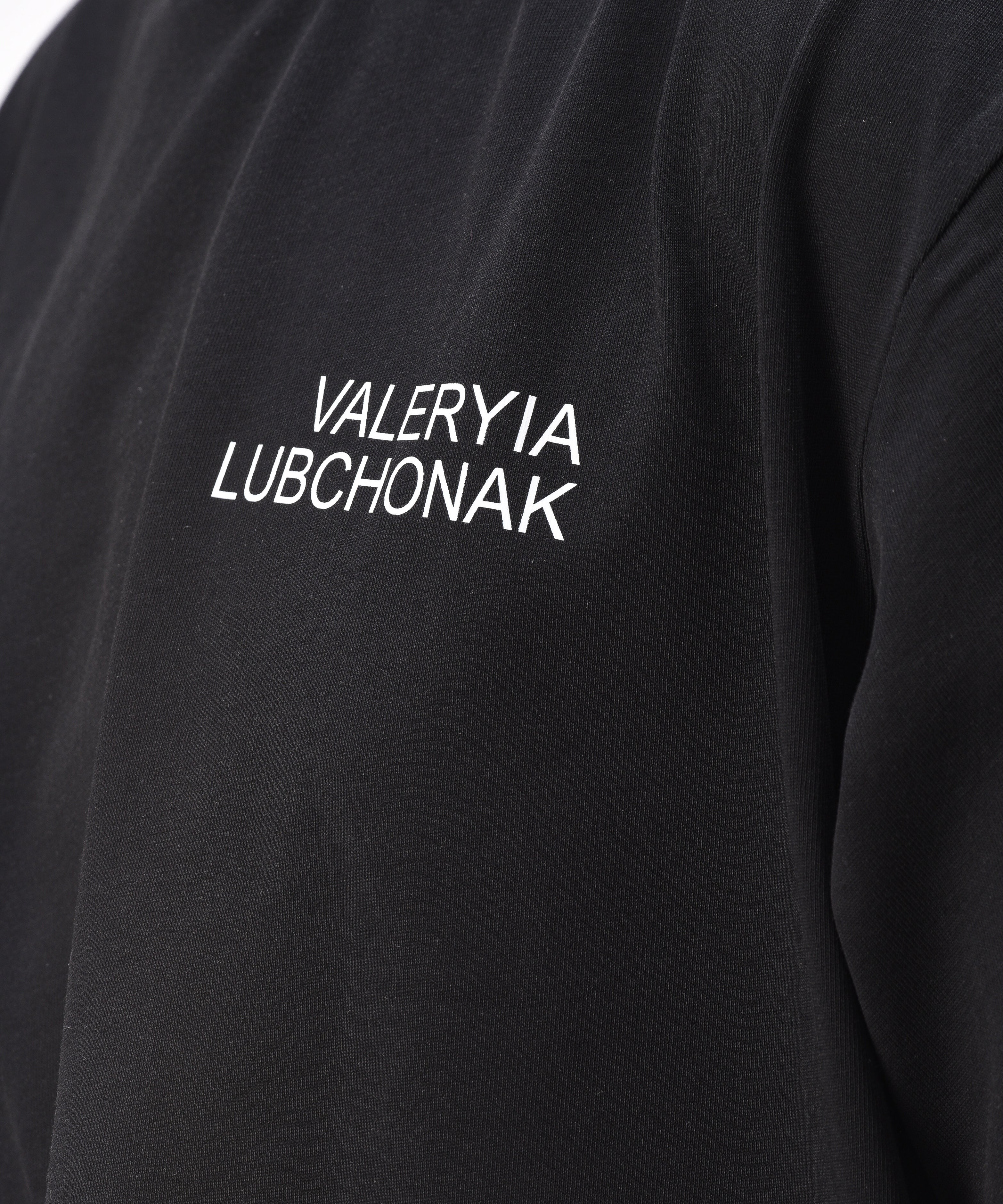 A black t-shirt with the words "Valeryia Lubchonak" on the left part of the top of the chest, and the "Lubchonak" logo on the bottom corner, close up.