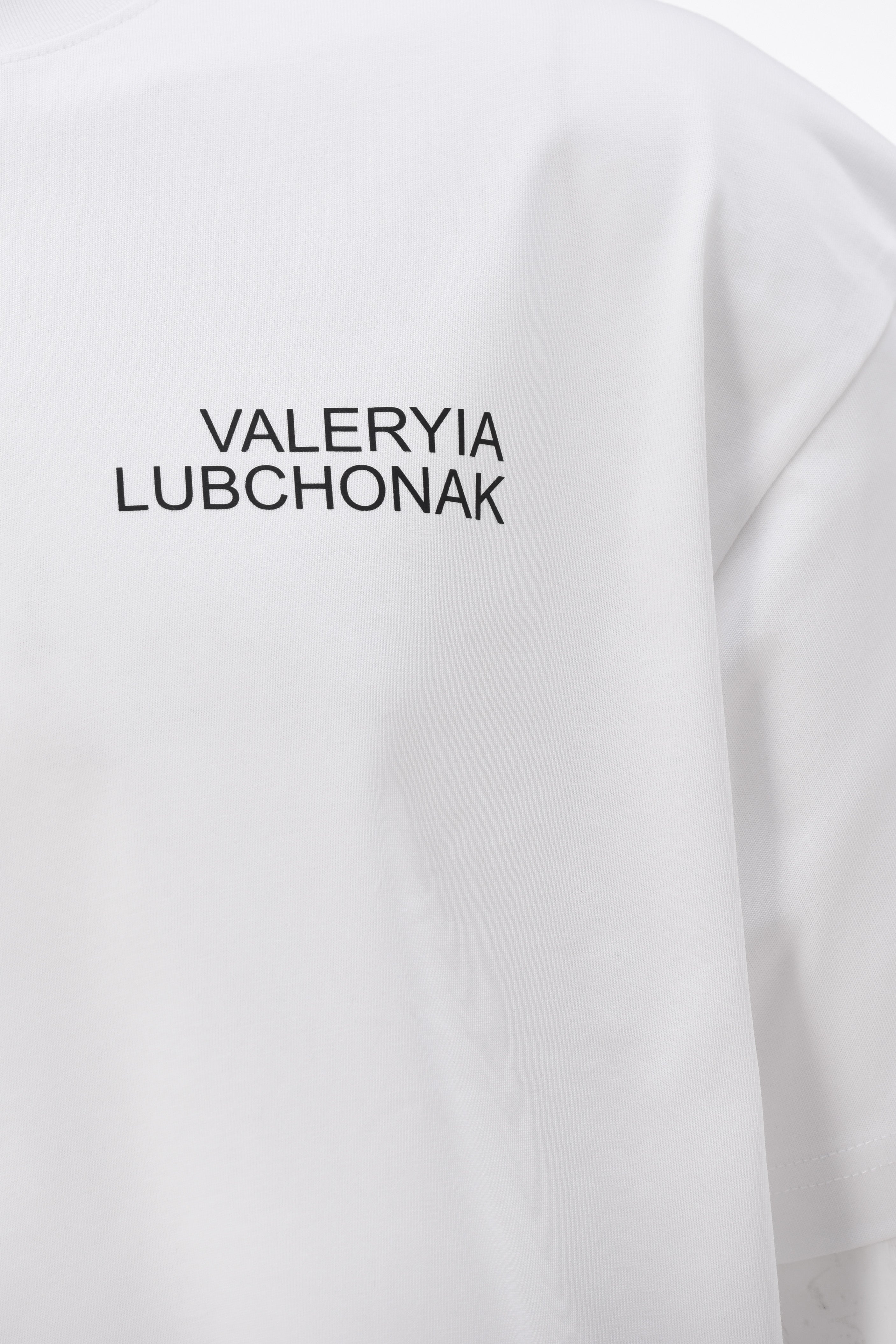 A black t-shirt with the words "Valeryia Lubchonak" on the left part of the top of the chest, and the "Lubchonak" logo on the bottom corner, close up.